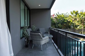 Un balcón con mobiliario de mimbre, una mesa de vidrio y vistas a una piscina y follaje.