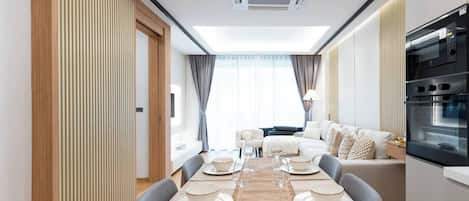 A modern dining area with a long table set for four, a sofa, and a kitchen with a built-in oven.