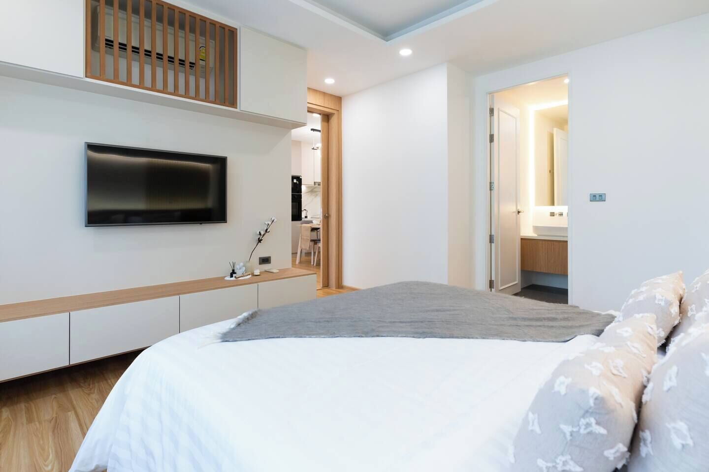 Un dormitorio con una cama, un televisor montado en la pared, un banco de madera y una puerta que da al baño.