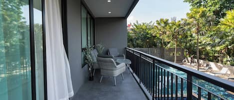 Un balcón con vistas a una piscina, una silla, una planta en maceta y una ventana con cortinas.