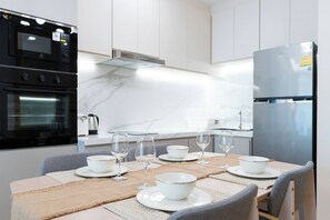 Eine moderne Küche mit integrierten Geräten, einer Marmor-Spritzschutzwand und einem Essbereich für sechs Personen, gedeckt mit weißem Geschirr.