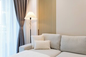 Une chambre d’hôtel moderne, équipée d’un canapé, de coussins, d’une lampe sur pied et d’une fenêtre avec des rideaux.