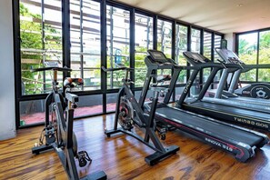 Un gimnasio con cintas de correr, elíptica y bicicleta estática, con amplios ventanales que dan a zonas verdes.