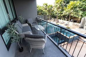 A balcony with wicker furniture, a glass table, and a view of a swimming pool and tropical plants. - Suite Coral 2br | Pool access|relife nai harn (Rawai)