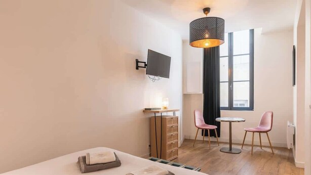 A hotel room with a bed, a desk, a chair, a TV, and a window.