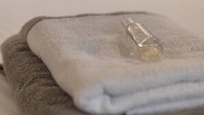 A neatly folded gray towel with a clear glass bottle on top, placed on a white surface.