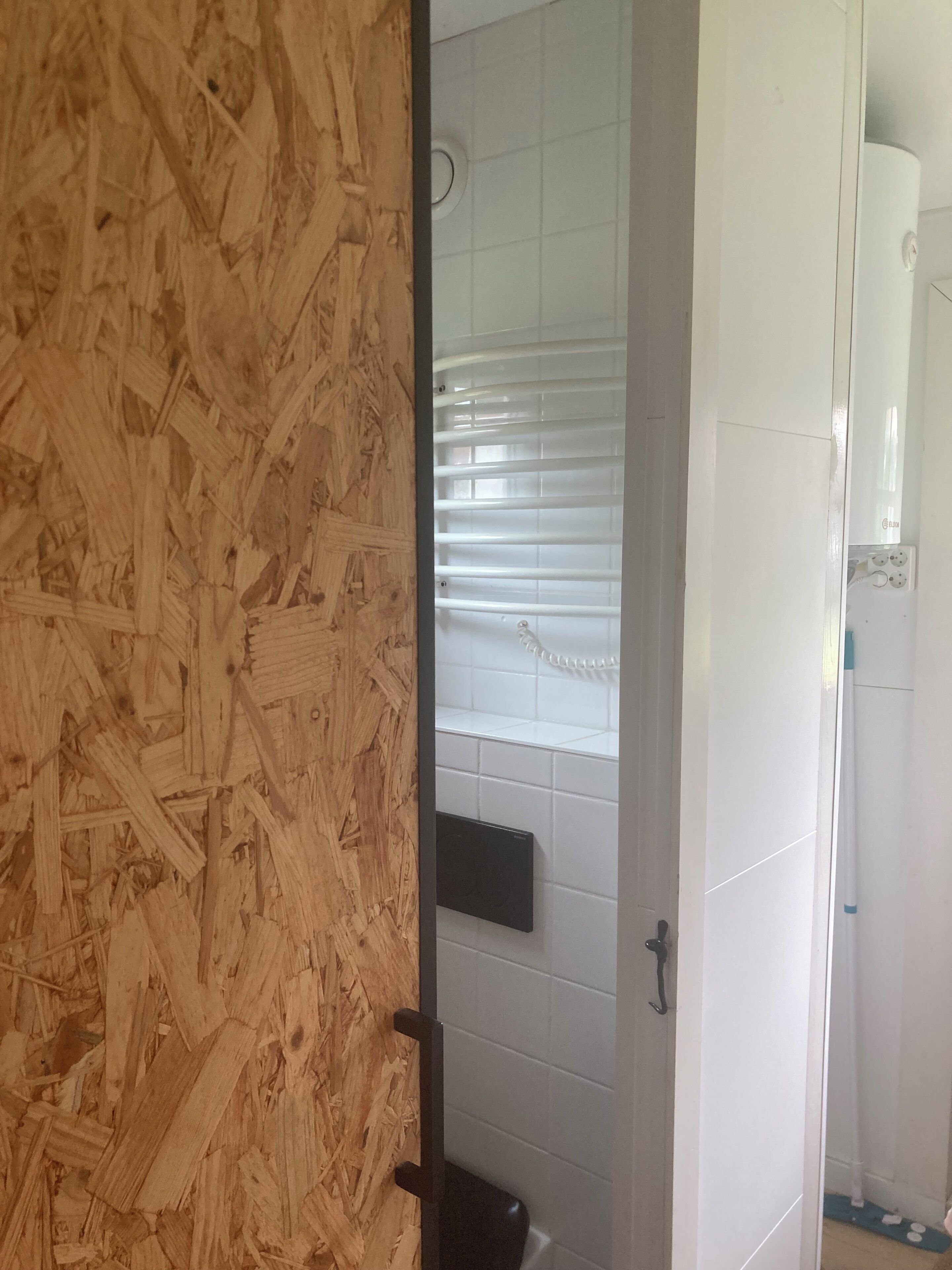 Une salle de bain avec des carreaux blancs, un mur en bois, des toilettes noires et un rideau de douche blanc.