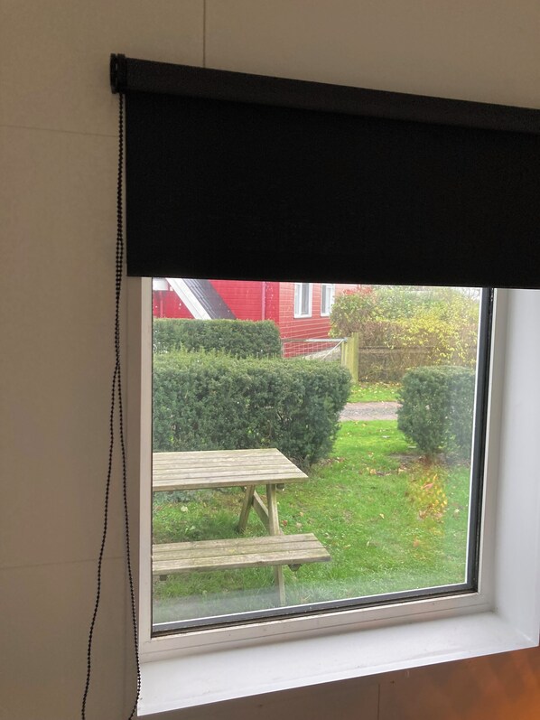 Una ventana con persiana negra, un banco de madera afuera y un edificio rojo al fondo.
