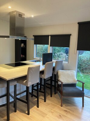 Una cocina moderna con estufa integrada, una zona de comedor con cuatro sillas y un ventanal con vistas a zonas verdes.