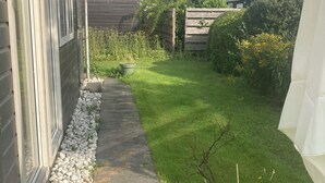 Un patio trasero residencial con un camino pavimentado, césped verde y una valla de madera.