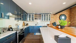 A modern kitchen with blue cabinets, a wooden countertop, and a brick wall. - Historic Bldg on Washington Blvd | Patio & BBQ (Ogden)