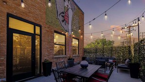 An outdoor patio with a brick wall, string lights, and a mural. - Historic Bldg on Washington Blvd | Patio & BBQ (Ogden)