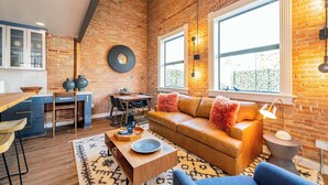 A cozy living room with a brick wall, a wooden dining table, and a sofa with cushions. - Historic Bldg on Washington Blvd | Patio & BBQ (Ogden)
