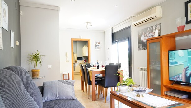 A modern living room with a grey sofa, wooden dining table, and a television.