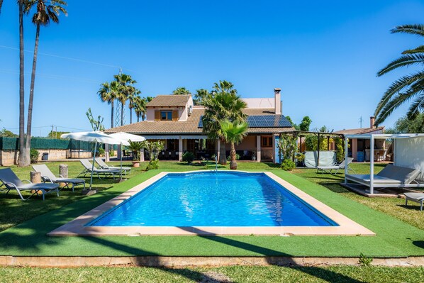 A swimming pool with lounge chairs, palm trees, and a house with a tiled roof.