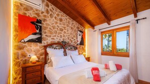A bedroom with a stone wall, a wooden ceiling, a bed with white bedding, a nightstand with a lamp, and a window with curtains. - Country House 'Ca Na Bisquerra' with Mountain View, Wi-Fi and Air Conditioning (Santa Margalida)