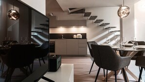 Un área de comedor moderna con un televisor de pantalla plana grande, una mesa de comedor con sillas y una cocina al fondo.