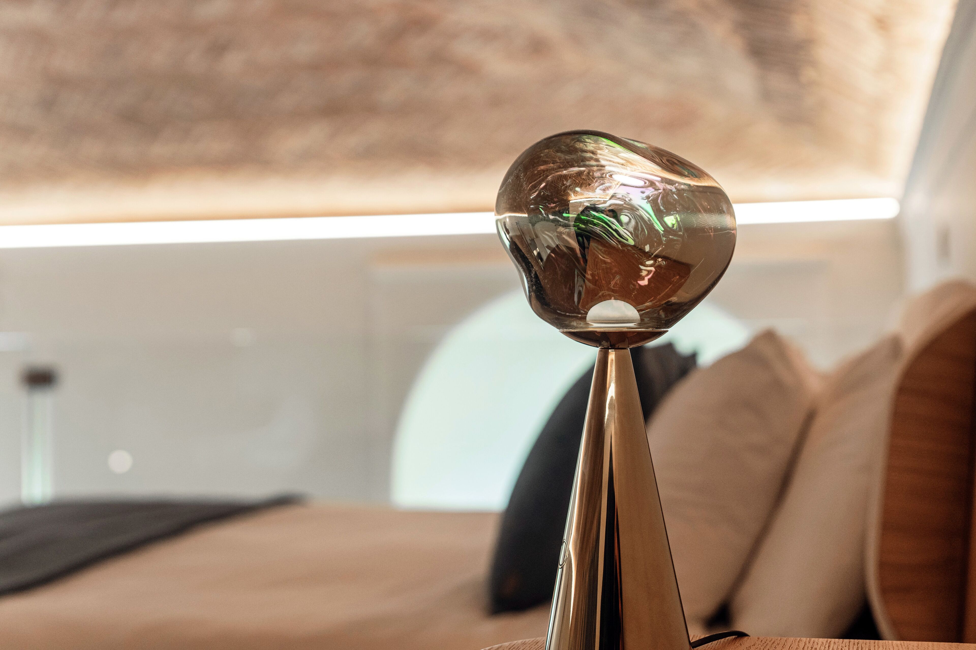 Un interno moderno con un oggetto sferico riflettente su un piedistallo, un divano con cuscini e una parete con motivo decorativo.