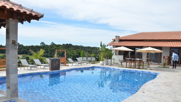 A swimming pool with tiled edges, lounge chairs, and umbrellas. - Chácara completa 5 quartos piscina, sauna, jacuzzi, churrasqueira e fogão lenha (Pouso Alegre)