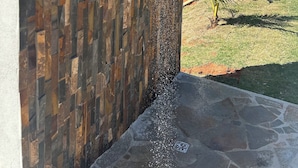 A stone shower wall with a waterfall feature, set against a clear blue sky. - Chácara completa 5 quartos piscina, sauna, jacuzzi, churrasqueira e fogão lenha (Pouso Alegre)