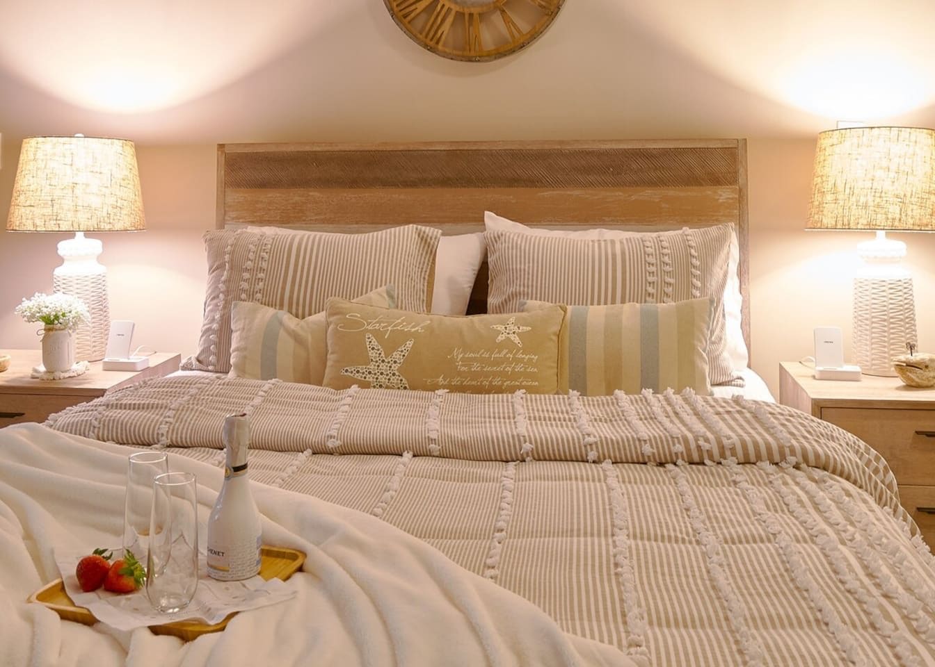 A neatly made bed with striped bedding, a bottle, and two glasses on a tray, accompanied by strawberries.