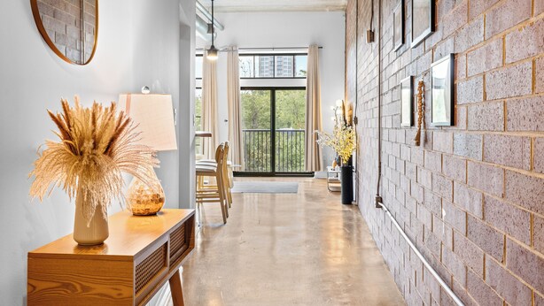 A hallway with a wooden console table, a vase with dried plants, a lamp, and a view of the outdoors through a large window. - Skyline Vibes, Walk to Stadium, Long Stay Ready (Charlotte)