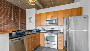 A modern kitchen with stainless steel appliances, wooden cabinets, and a brick wall. - Skyline Vibes, Walk to Stadium, Long Stay Ready (Charlotte)