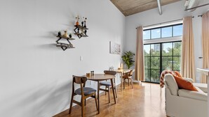 A modern living room with a dining area, large windows, and a view of greenery outside. - Skyline Vibes, Walk to Stadium, Long Stay Ready (Charlotte)