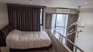 A modern hotel room with a large bed, a nightstand, a desk, and a balcony with a railing and a view of the city.