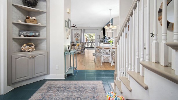 A spacious hallway with a wooden floor, a patterned rug, and a staircase with white balusters.
