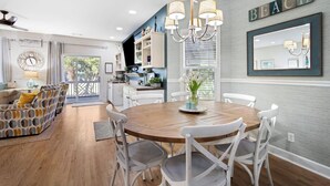 A modern kitchen with white cabinets, a wooden dining table, and a chandelier.