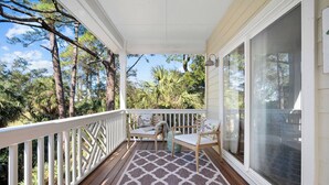 A covered porch with a patterned rug, wooden chairs, and a view of trees and foliage.