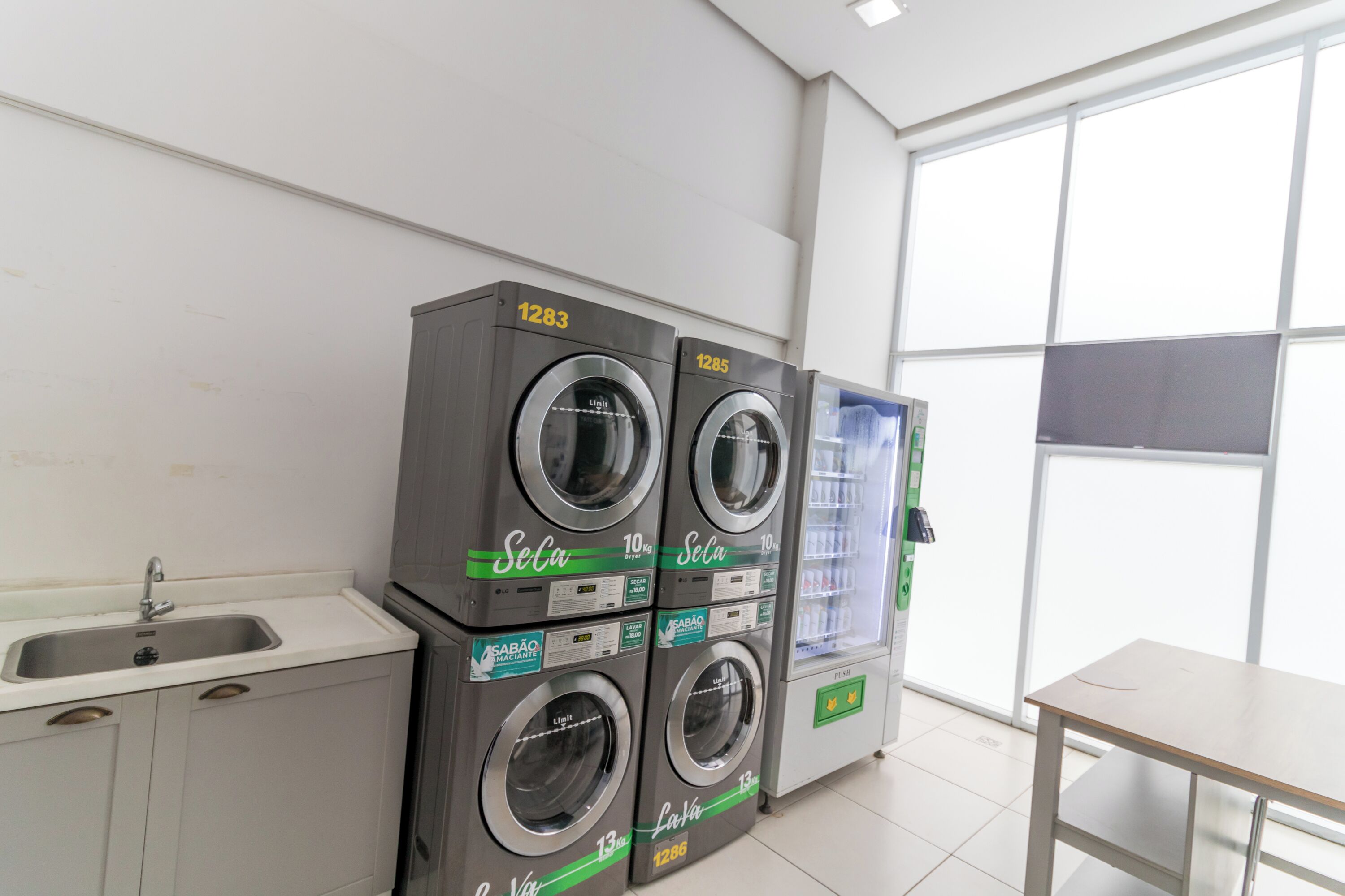 A laundry facility with four washing machines, a sink, and a vending machine.