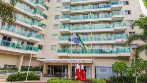 A high-rise residential building with multiple balconies, a landscaped entrance area, and a flagpole with a flag.