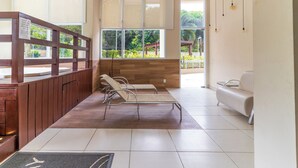A reception area with a wooden reception desk, two lounge chairs, a white sofa, and large windows with a view of greenery outside.