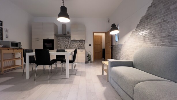 A modern kitchen with white cabinets, a dining table with chairs, and a grey sofa.