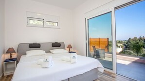Een moderne slaapkamer met een groot bed, twee nachtkastjes en een glazen schuifdeur naar een balkon.