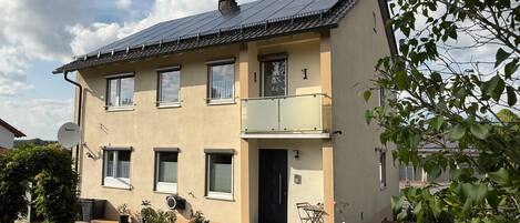 Een gebouw met twee verdiepingen, een balkon, een schotelantenne en een kleine tuin.