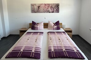 Ein Doppelbett mit einem gemusterten Bettbezug, zwei Nachttische mit Lampen, ein an der Wand befestigtes Kunstwerk und ein Holzboden.