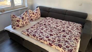 Una cama con colcha estampada, dos almohadas y una mesita de noche en una habitación con ventana.