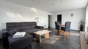 Un salon moderne avec un canapé gris, une table basse en bois et un coin repas comprenant des chaises et une table.