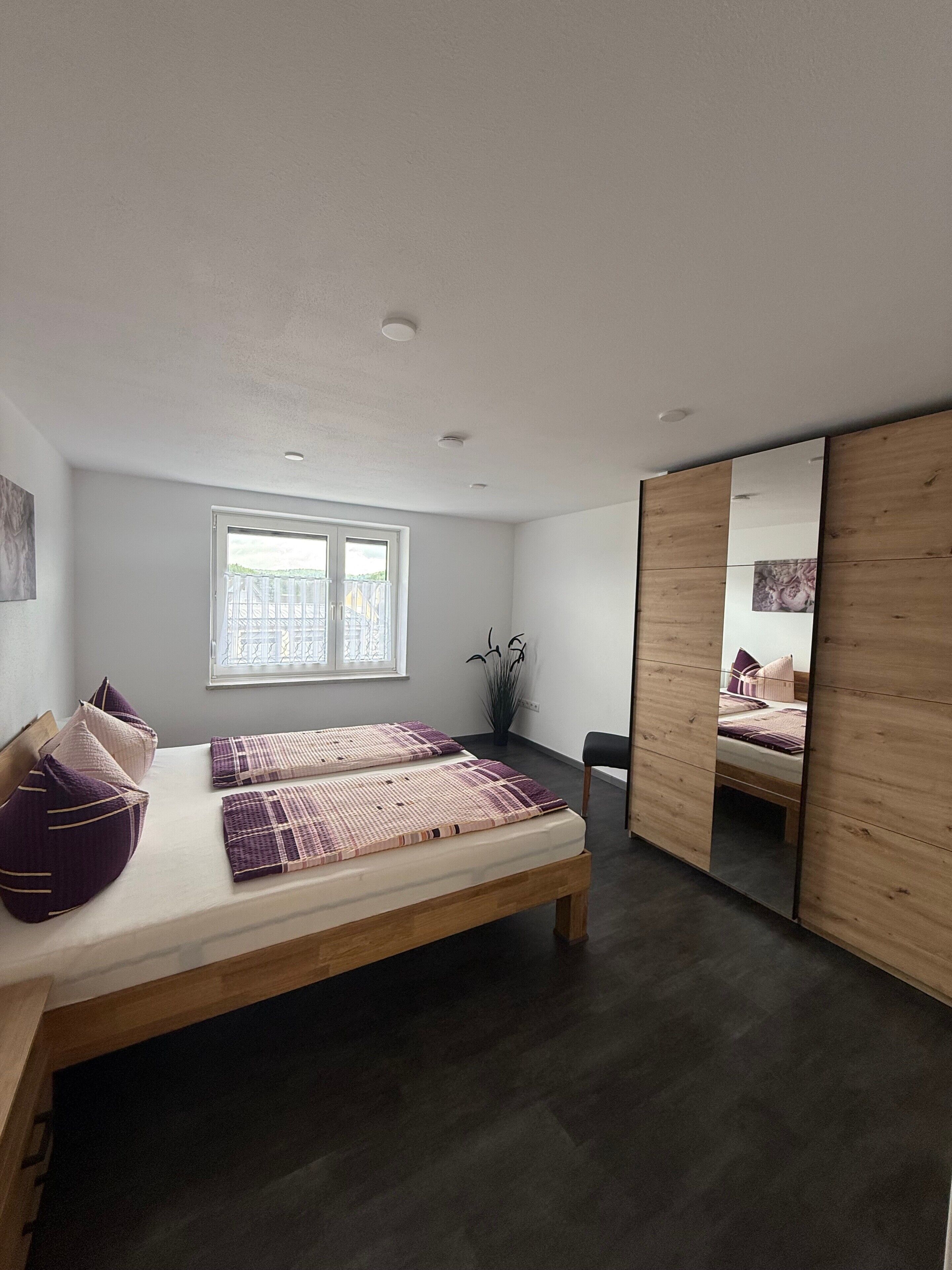 A modern bedroom with a large bed, a window, and a mirror.