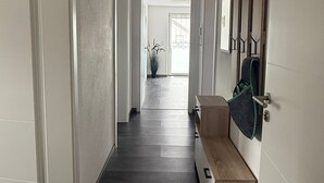 Un couloir avec un banc en bois, des murs blancs et une porte sur le côté gauche.
