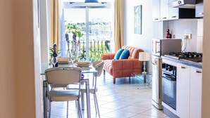 A modern kitchen with a dining area, a sofa with cushions, and a view of the city through large windows. - Cosy Apartment with Valletta and Harbour Views (Sliema)