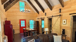 Ein gemütliches Blockhaus mit Holzvertäfelung, einer roten Tür, einer Essecke und einem Ledersofa.