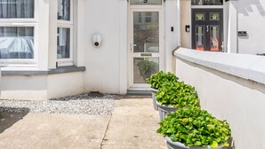 Un edificio blanco con puerta número 9, una cámara de seguridad y plantas en macetas a lo largo del camino.
