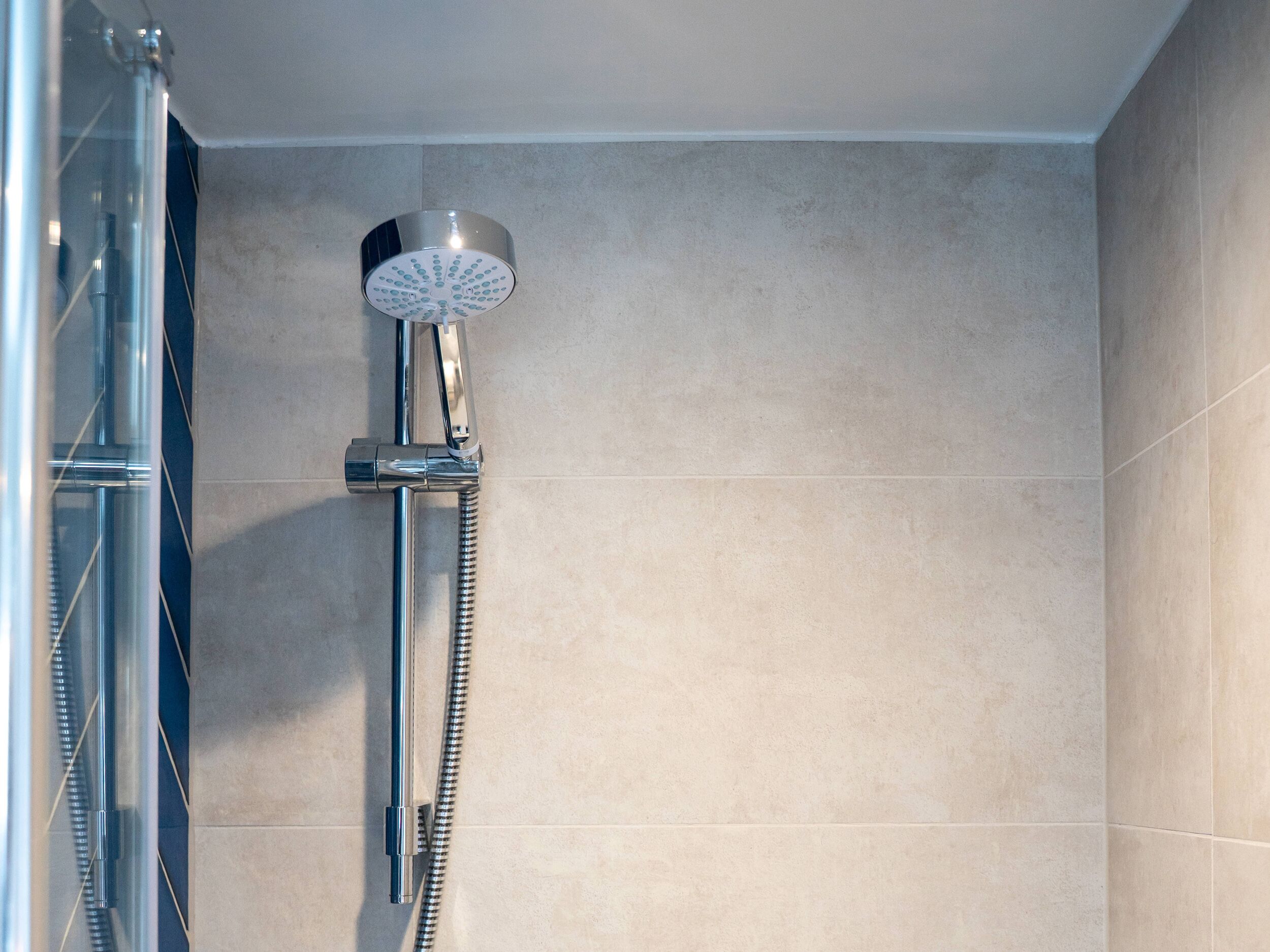Ducha con cabezal de ducha de mano y manguera flexible, instalada en una pared con suelo de azulejos.