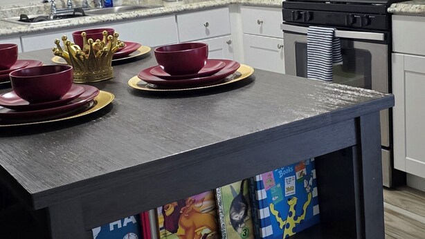 Une cuisine avec des meubles blancs, un four à micro-ondes, une cuisinière et un plan de travail noir agrémenté de bols et d’assiettes rouges.