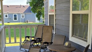Une véranda couverte, avec quatre fauteuils en osier et une petite table, donnant sur une pelouse et une maison.