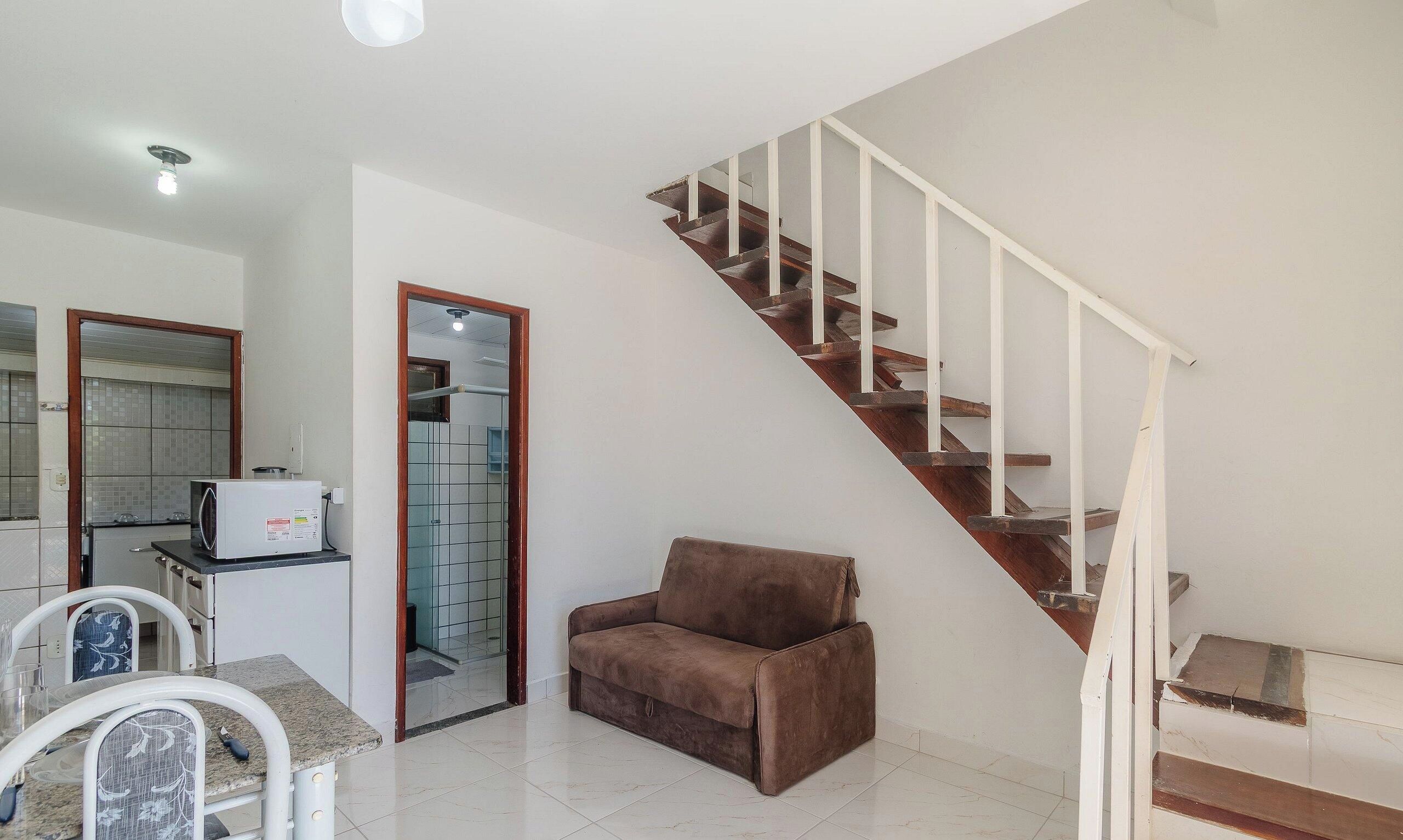 A kitchen with a microwave, a dining table with chairs, and a brown sofa. There is a staircase with wooden steps and white railings.